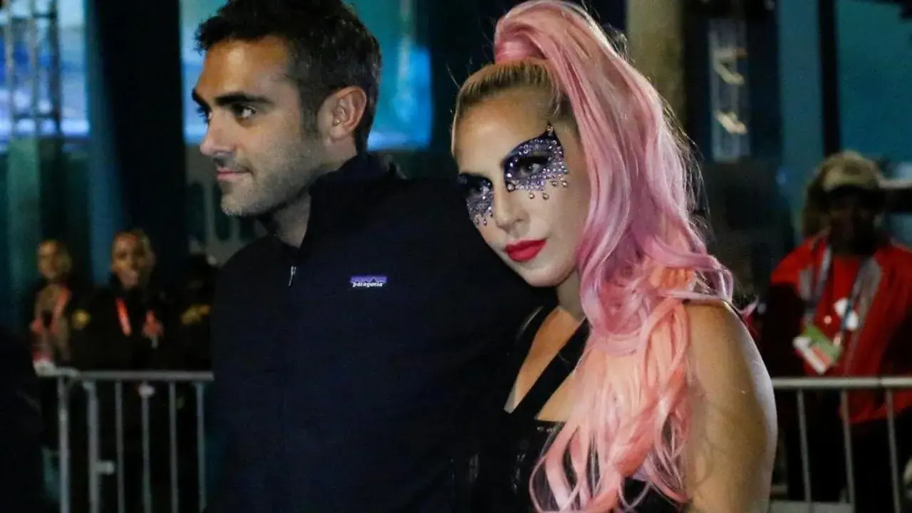 Lady Gaga con il suo fidanzato, Christian Carino, durante un evento. Lei indossa un trucco scintillante e capelli rosa.