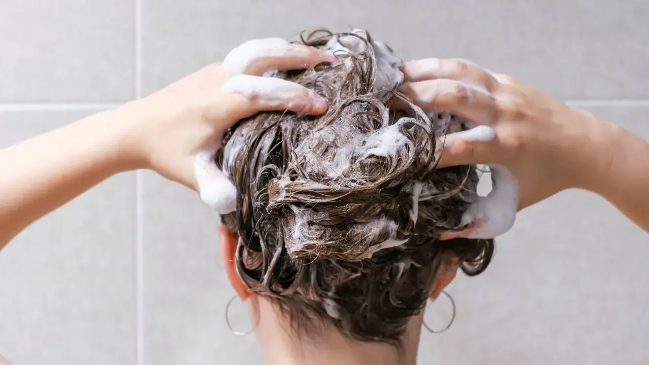 Mani che massaggiano shampoo sui capelli bagnati, schiuma abbondante. La domanda "ogni quanto lavare i capelli" è centrale per una chioma sana.