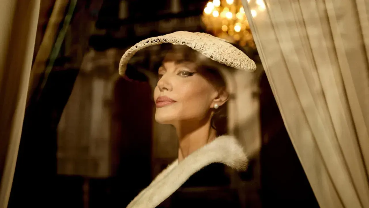 Angelina Jolie nei panni di Maria Callas, con un cappello di pizzo e una pelliccia, evoca l'eleganza di un'epoca passata.