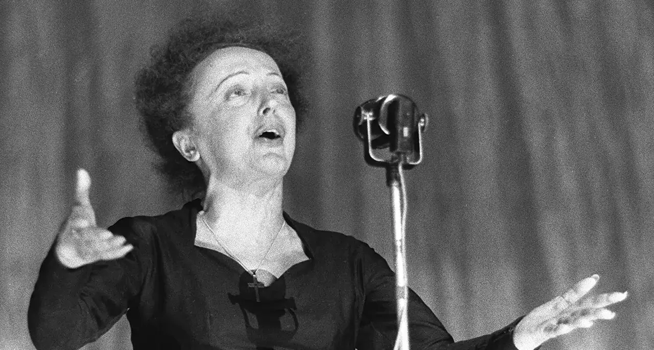 La leggendaria Édith Piaf canta con passione, la sua voce risuona mentre il pubblico immagina la sua causa morte.