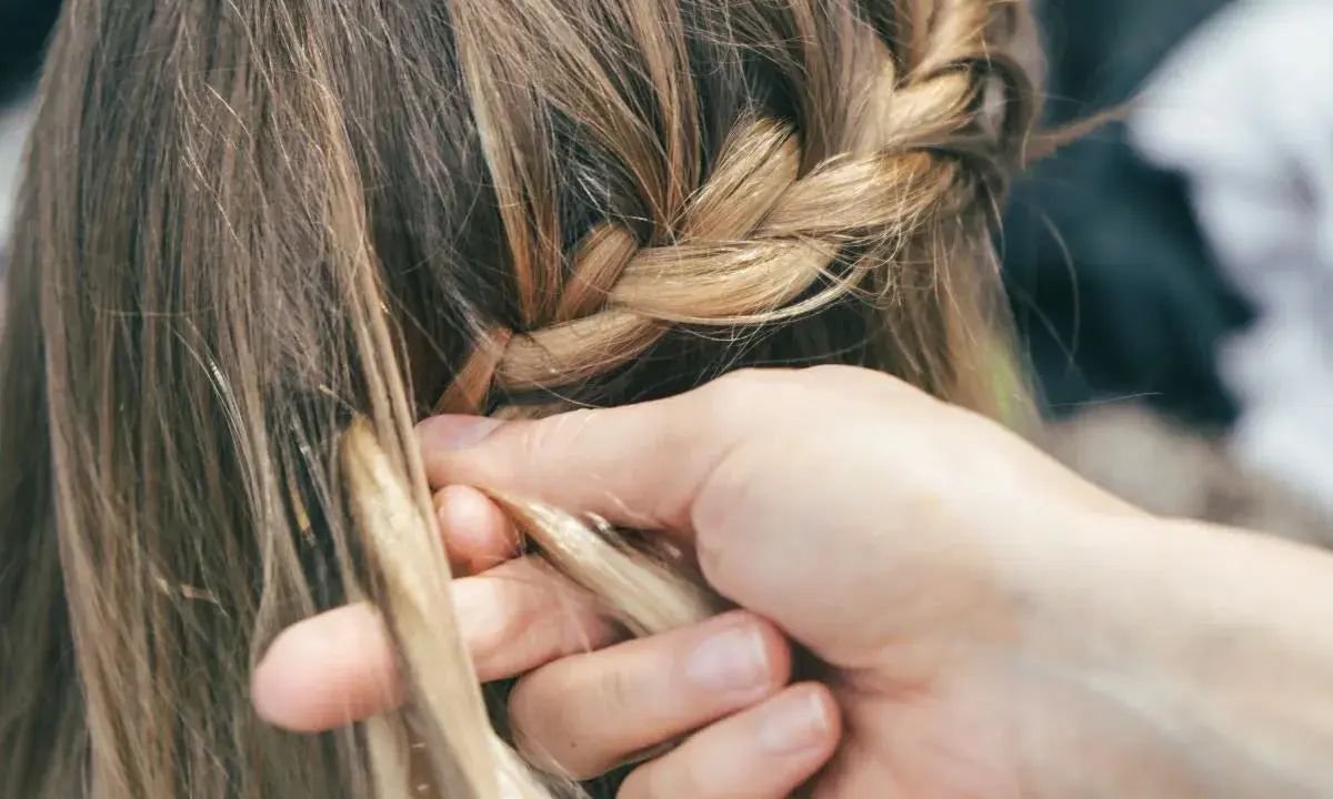 Mani esperte creano trecce alla francese, intrecciando ciocche bionde con cura.