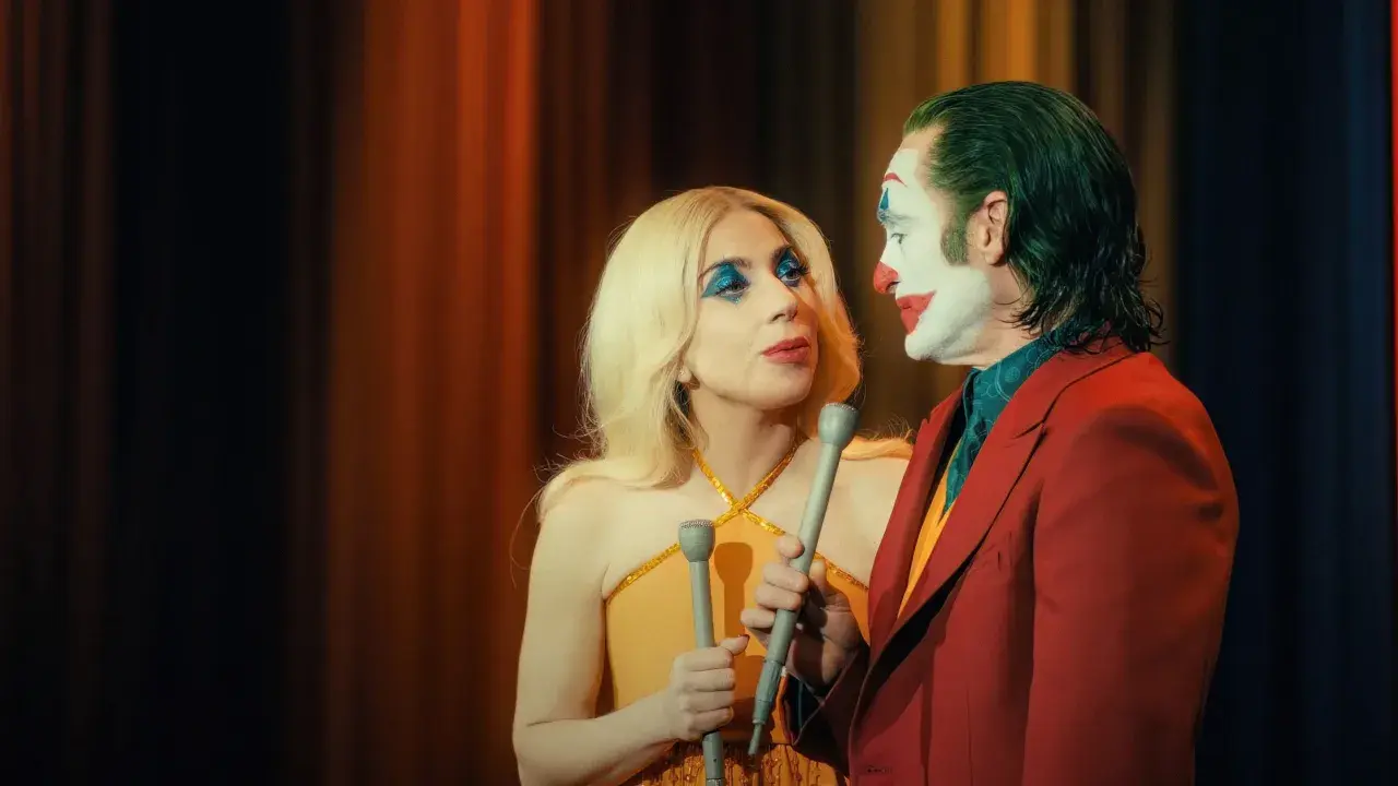Joker e Harley Quinn, uniti dalla follia, si guardano intensamente. Lui con il trucco iconico, lei con un look scintillante. Joker folie a deux.