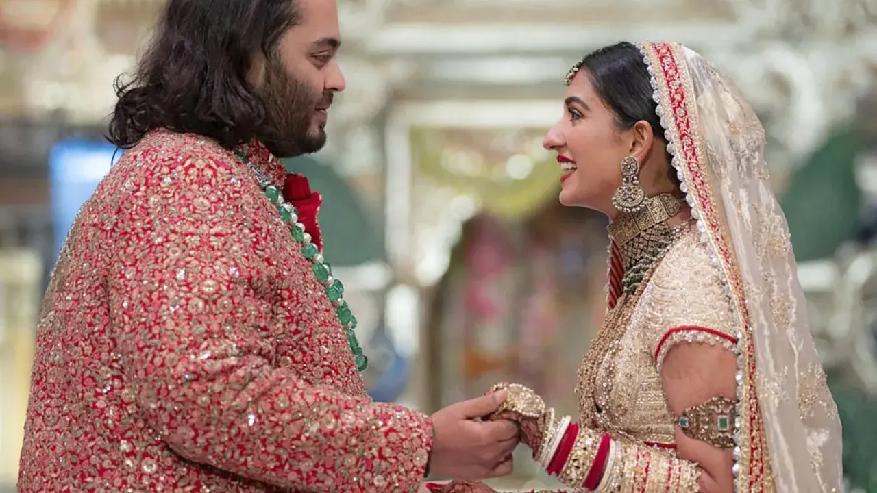 Anant Ambani matrimonio: la sposa sorride guardando lo sposo, entrambi vestiti con abiti tradizionali riccamente decorati.