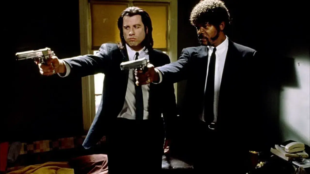 Due uomini in abito scuro puntano pistole, iconica scena da un film anni 90.