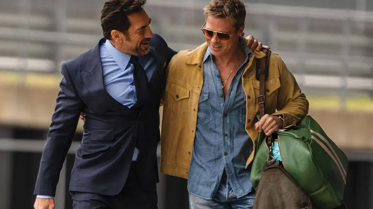 Brad Pitt 2024, con giacca gialla e camicia di jeans, cammina con un amico in completo scuro.