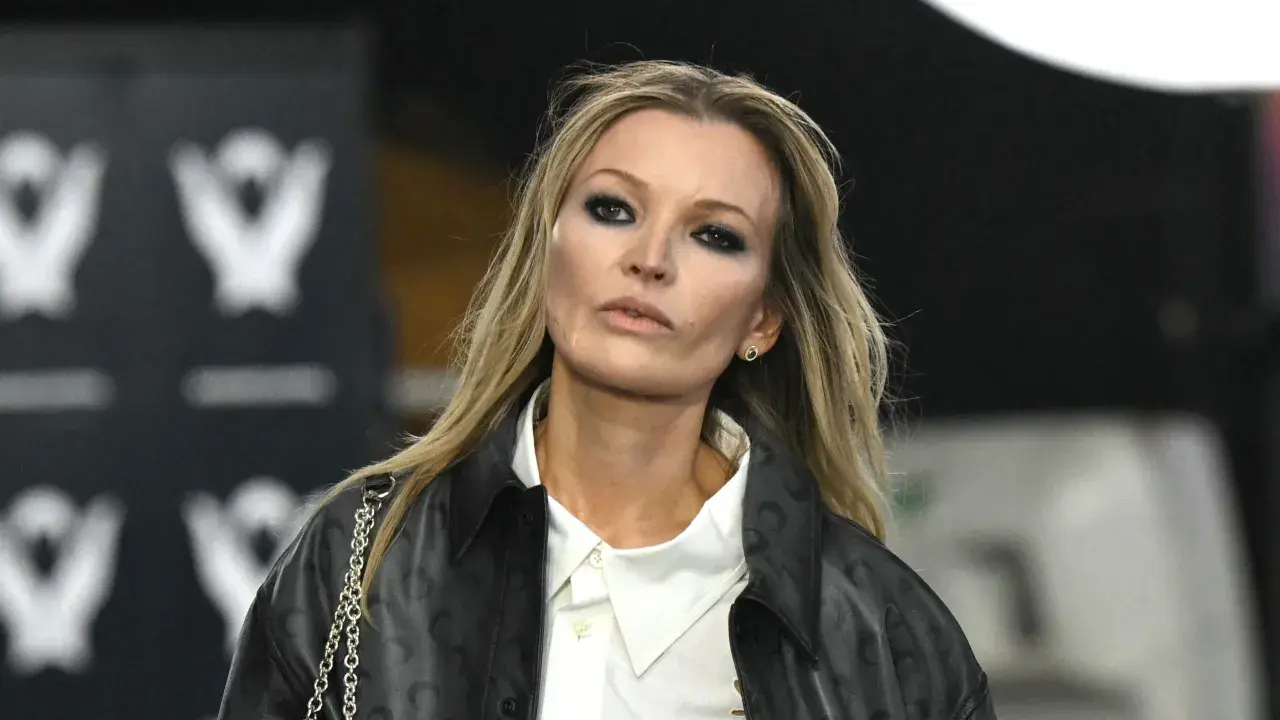 Kate Moss oggi, con un look audace e un trucco marcato, sfila con un giubbotto di pelle e una camicia bianca.