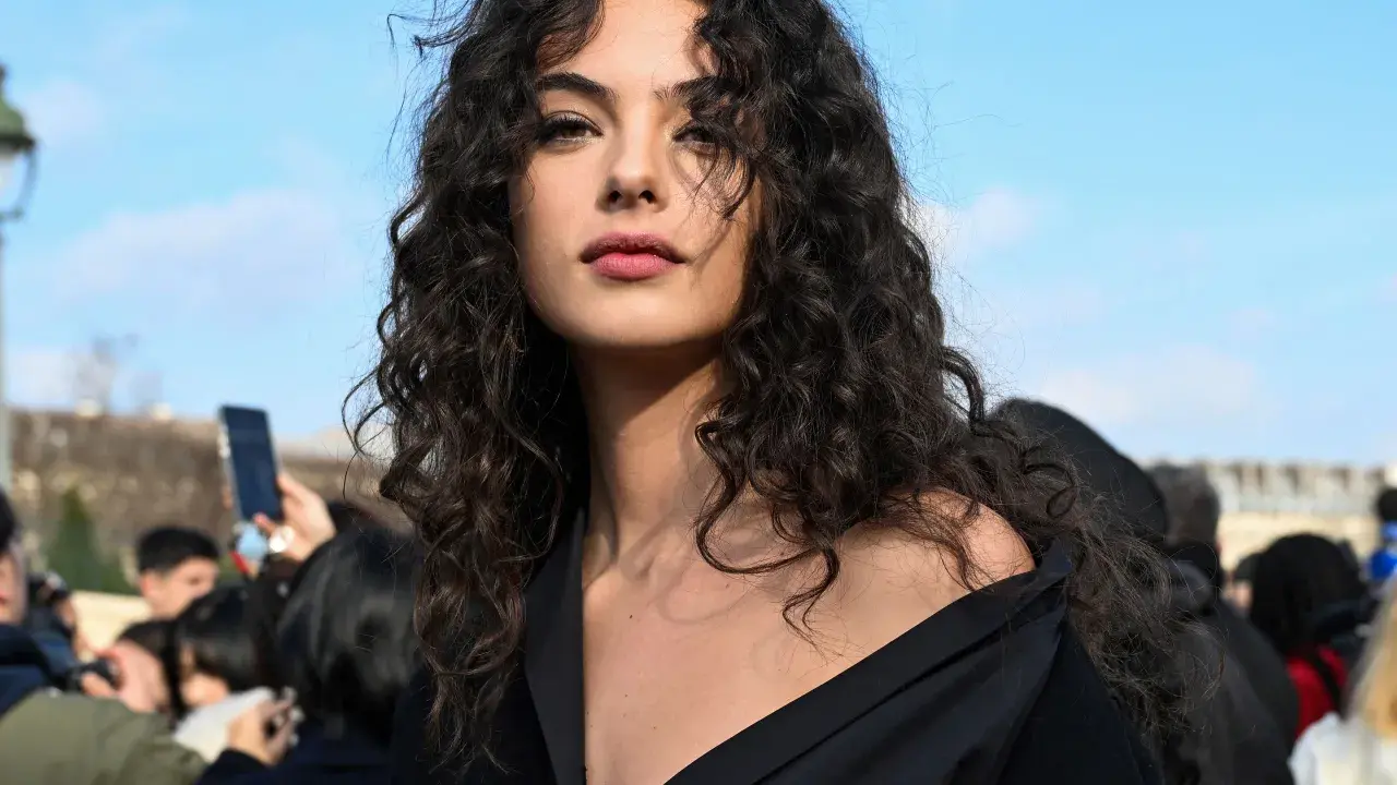 Ragazza con splendidi capelli ricci naturali con frangia, che incorniciano un viso intenso sotto un cielo azzurro.
