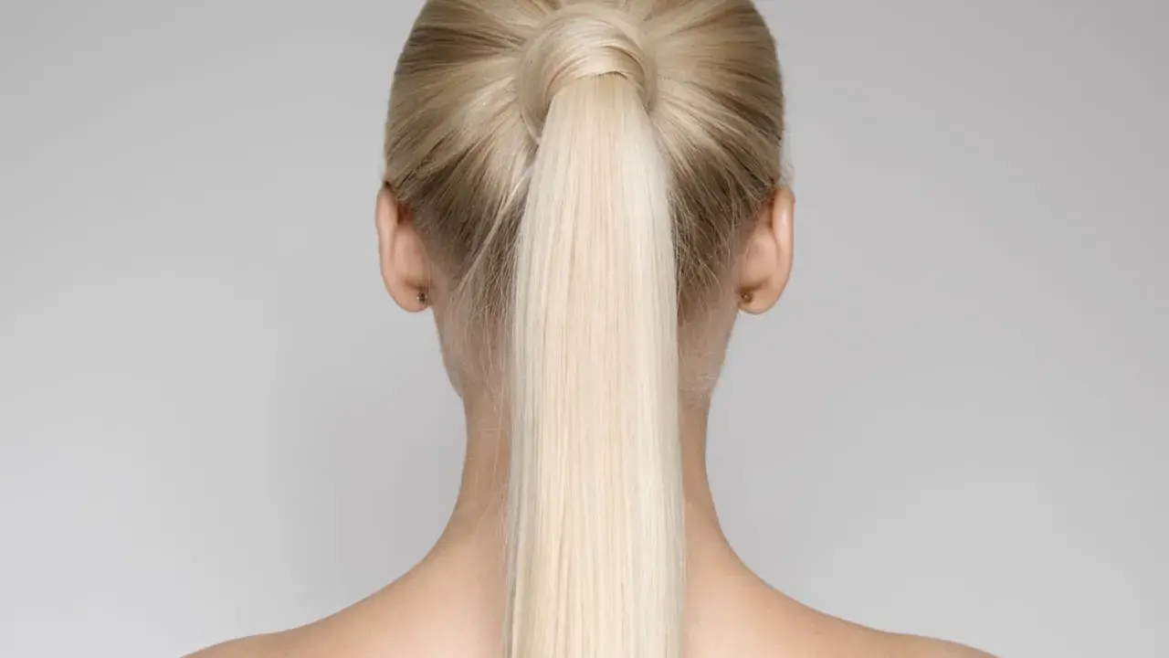 Vista posteriore di una donna con una **coda alta gonfia davanti**, capelli biondi lisci e spalle scoperte.