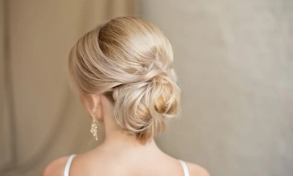 Chignon basso cerimonia con capelli biondi intrecciati, un'acconciatura elegante e raffinata per un'occasione speciale.
