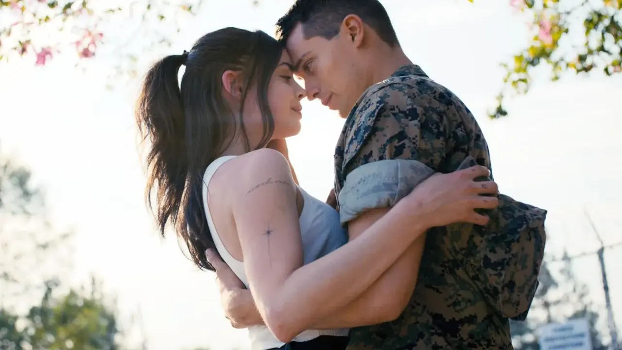 Nicholas Galitzine, in uniforme militare, abbraccia teneramente la sua fidanzata sotto un albero fiorito.