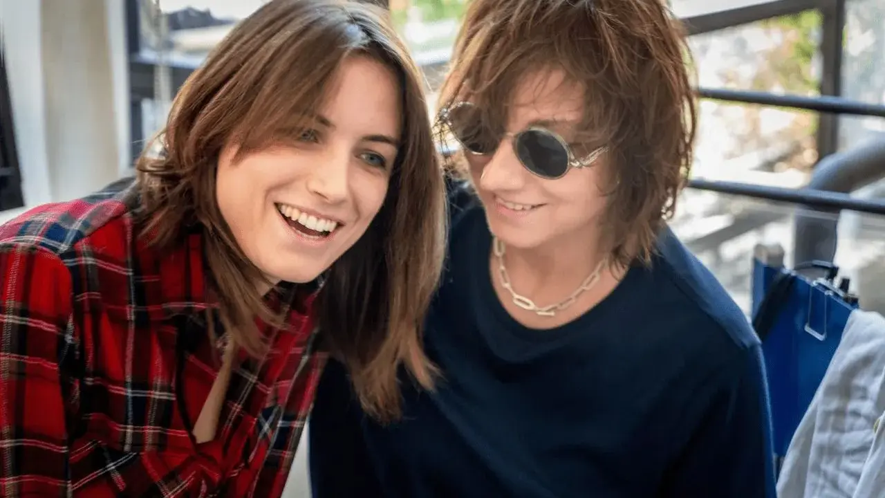 Due donne sorridono, una con camicia a quadri rossi, l'altra con occhiali da sole. Potrebbero essere Gianna Nannini e la sua moglie.
