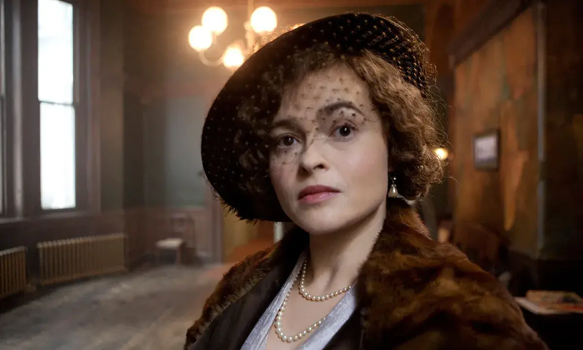 Helena Bonham Carter, con cappello e velo, indossa una pelliccia e perle. Scena da un film.