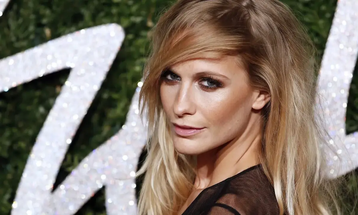Donna con capelli sciolti eleganti, sguardo intenso e trucco deciso, sullo sfondo di un logo scintillante.