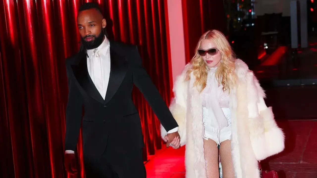 Madonna, con un cappotto di pelliccia bianco e un abito audace, cammina mano nella mano con il suo compagno, vestito elegantemente in smoking nero.