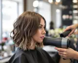 Donna con un taglio scalato medio corto, mentre il parrucchiere le asciuga i capelli con un phon.