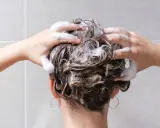 Mani che massaggiano shampoo sui capelli bagnati, schiuma abbondante. La domanda "ogni quanto lavare i capelli" è centrale per una chioma sana.
