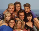 Il cast di Beverly Hills 90210, un gruppo di amici sorridenti con lo sfondo del mare.