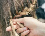 Mani esperte creano trecce alla francese, intrecciando ciocche bionde con cura.