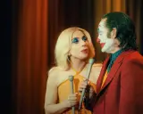 Joker e Harley Quinn, uniti dalla follia, si guardano intensamente. Lui con il trucco iconico, lei con un look scintillante. Joker folie a deux.