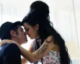 Blake Fielder-Civil, marito di Amy Winehouse, la bacia teneramente. Lei ha i capelli neri raccolti e indossa un top con ancore.