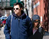 Harry Styles e la sua fidanzata passeggiano per strada, lui con occhiali bianchi, lei al telefono con un cappellino "KISS".
