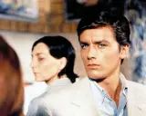 Alain Delon, icona di stile, in una scena che evoca i suoi film più belli. Sguardo intenso, fascino intramontabile.