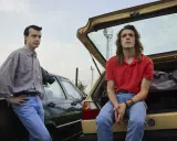 Due ragazzi in jeans e camicie, appoggiati a due auto d'epoca. Scena dalla serie tv 883.