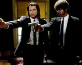 Due uomini in abito scuro puntano pistole, iconica scena da un film anni 90.