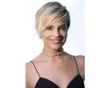 Donna con capelli cortissimi biondi, look 2026, indossa un abito nero e collane scintillanti.
