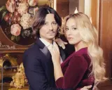 Francesca Manzini e il suo fidanzato, un abbraccio elegante davanti a un quadro di fiori e un orologio dorato.