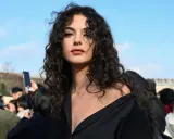 Ragazza con splendidi capelli ricci naturali con frangia, che incorniciano un viso intenso sotto un cielo azzurro.