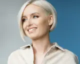 Donna sorridente con capelli sottili e pochi, taglio corto biondo platino e un orecchino a grappolo.