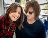 Due donne sorridono, una con camicia a quadri rossi, l'altra con occhiali da sole. Potrebbero essere Gianna Nannini e la sua moglie.