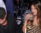 Vittoria Ceretti e Leonardo DiCaprio sorridono a una cena. Lei tiene un bicchiere, lui indossa un cappellino con la "LA".