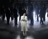 Achille Lauro, vestito di bianco, canta sul palco circondato da un coro in controluce, un'immagine che evoca un sentimento di essere perdutamente innamorato.