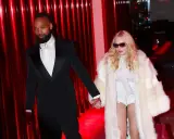 Madonna, con un cappotto di pelliccia bianco e un abito audace, cammina mano nella mano con il suo compagno, vestito elegantemente in smoking nero.