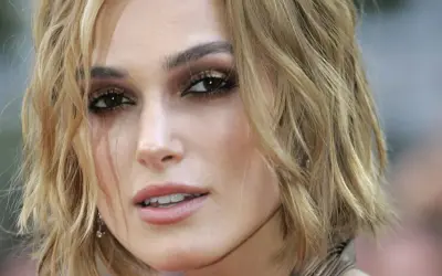 Primo piano di una donna con taglio butterfly capelli corti biondi, trucco occhi intenso e labbra rosa.