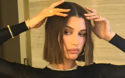 Modello con capelli castani, lisci e pochi, che sfoggia un taglio a caschetto. Indossa gioielli d'oro e un abito nero.