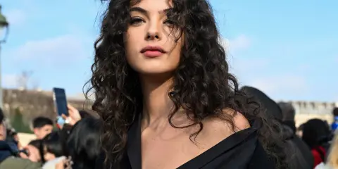 Ragazza con splendidi capelli ricci naturali con frangia, che incorniciano un viso intenso sotto un cielo azzurro.
