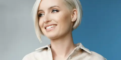 Donna sorridente con capelli sottili e pochi, taglio corto biondo platino e un orecchino a grappolo.