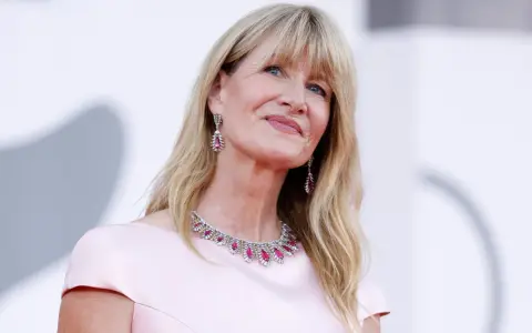 L'attrice bionda americana Laura Dern sorride con un abito rosa e gioielli scintillanti.