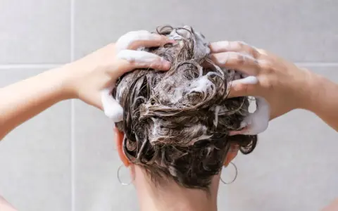 Mani che massaggiano shampoo sui capelli bagnati, schiuma abbondante. La domanda "ogni quanto lavare i capelli" è centrale per una chioma sana.