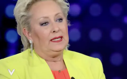 Carolyn Smith, come sta, con un tailleur giallo acceso e un top arancione, parla con un microfono.