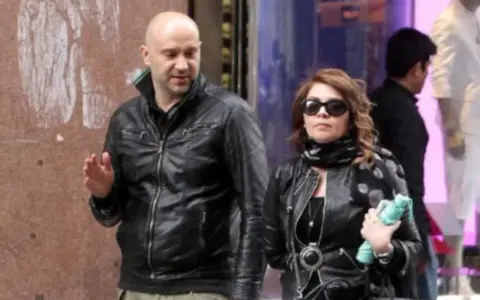 Cristina D'Avena passeggia con quello che sembra essere il suo marito, entrambi vestiti di pelle nera.
