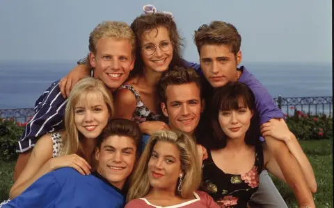 Il cast di Beverly Hills 90210, un gruppo di amici sorridenti con lo sfondo del mare.