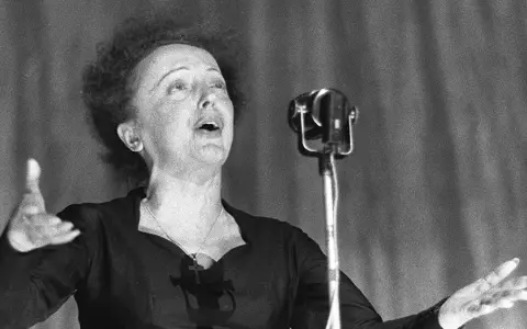 La leggendaria Édith Piaf canta con passione, la sua voce risuona mentre il pubblico immagina la sua causa morte.