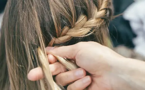 Mani esperte creano trecce alla francese, intrecciando ciocche bionde con cura.