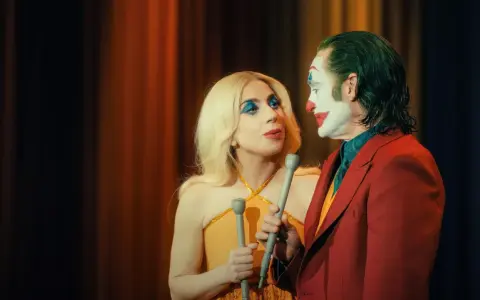 Joker e Harley Quinn, uniti dalla follia, si guardano intensamente. Lui con il trucco iconico, lei con un look scintillante. Joker folie a deux.