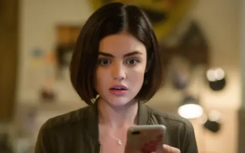 Lucy Hale, protagonista di film e programmi TV, guarda sorpresa il suo telefono.