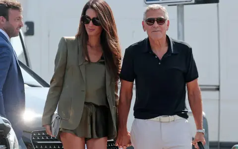 Amal Clooney, con il suo impeccabile fisico, passeggia mano nella mano con George Clooney, entrambi sorridenti e alla moda.